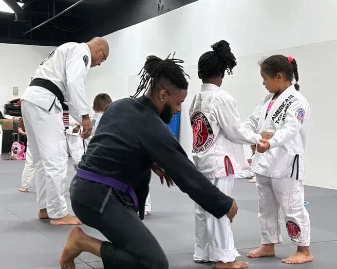 Coaches help young students tie their belts during a kids class.