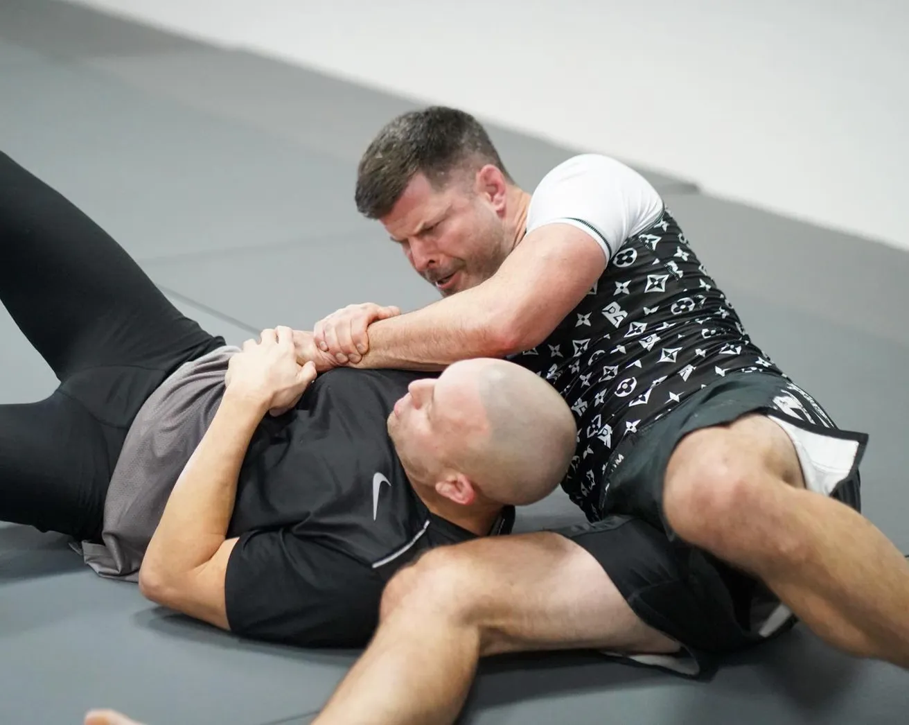Two adults on the mat, one controlling the other’s arm from the top position.